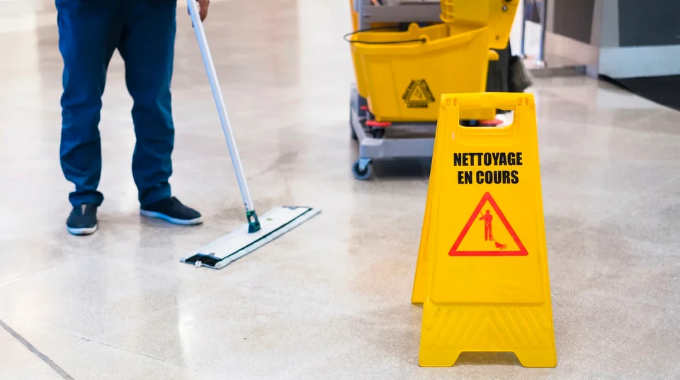 Sc&egrave;ne int&eacute;rieure de nettoyage professionnel avec agent d'entretien en uniforme blanc maniant un chariot de m&eacute;nage