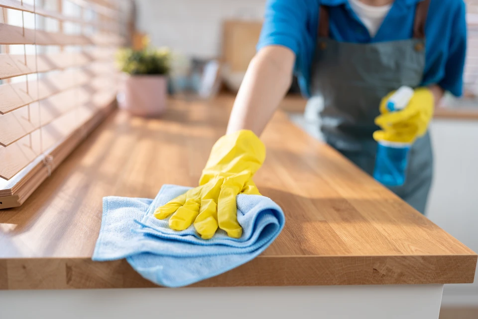 Intérieur résidentiel moderne montrant une personne effectuant un nettoyage professionnel d'un salon ou d'une cuisine. L'image doit présenter un espace habitable domestique propre et lumineux, avec la professionnelle utilisant du matériel de nettoyage adapté, illustrant un service de qualité dans le cadre d'un ménage à domicile professionnel et déclaré.